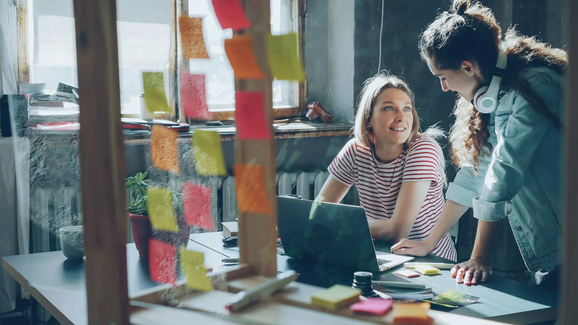 Two people talking at a desk, seen through a glass pane covered in colorful sticky notes