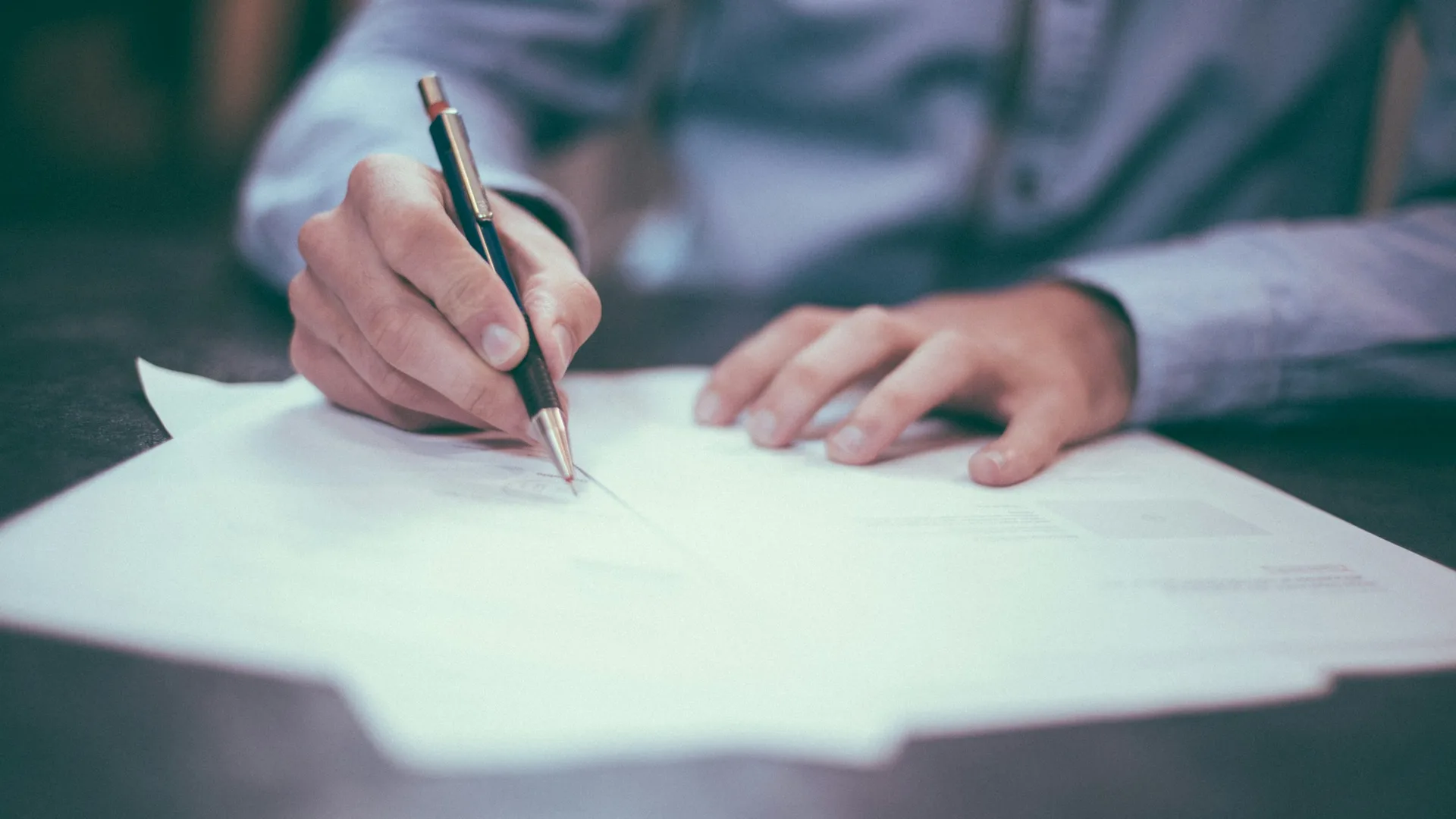 Hands filling out a printed form with a pen, translating information from paper into a record