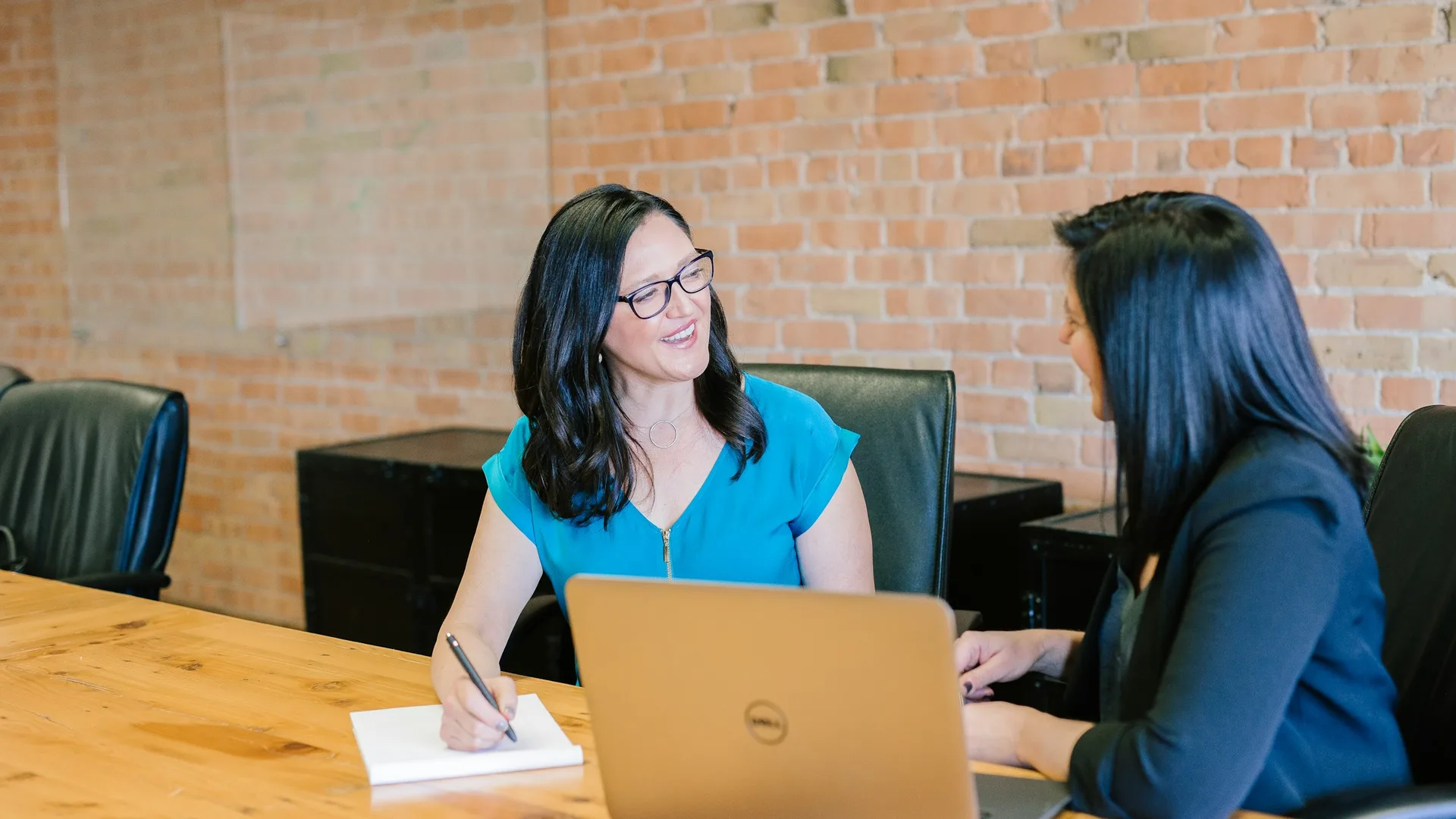 Two people talking across a table with a laptop and a notepad, a working review rather than a confrontation